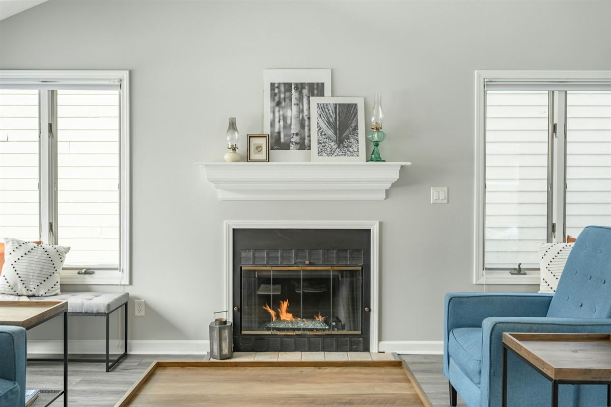 A bright living room with white plantation shutters, a fireplace and blue armchairs
