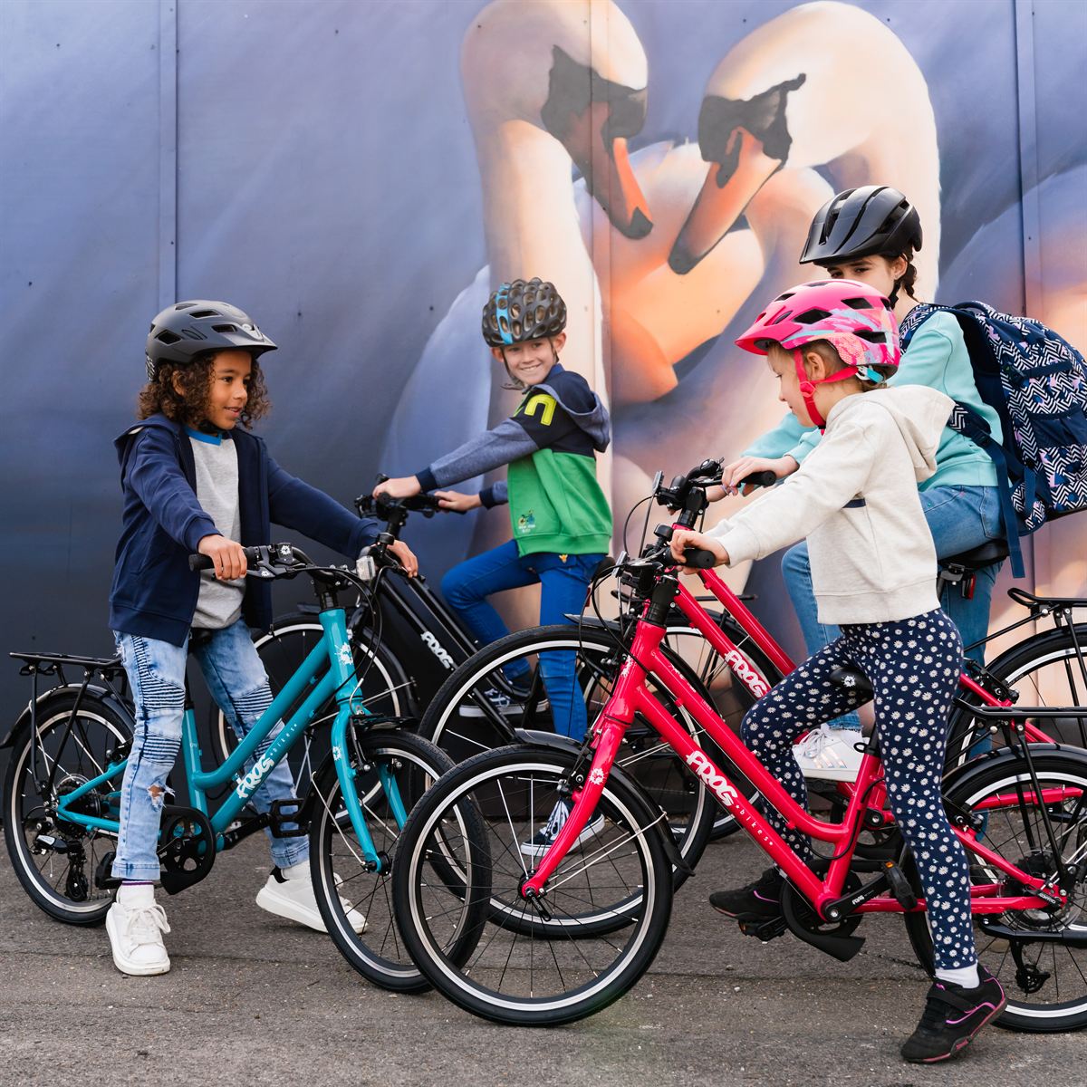 Children riding Frog bikes in front of a mural